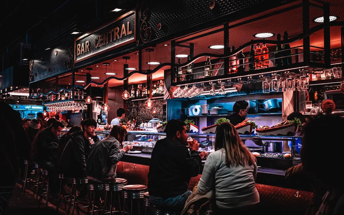 Des clients assis au comptoir d’un bar-restaurant éclairé en soirée.