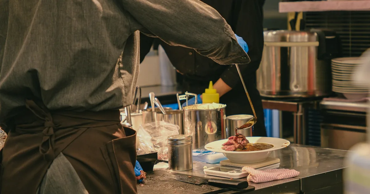 Des cuisiniers préparent les aliments devant un plan de travail en cuisine.