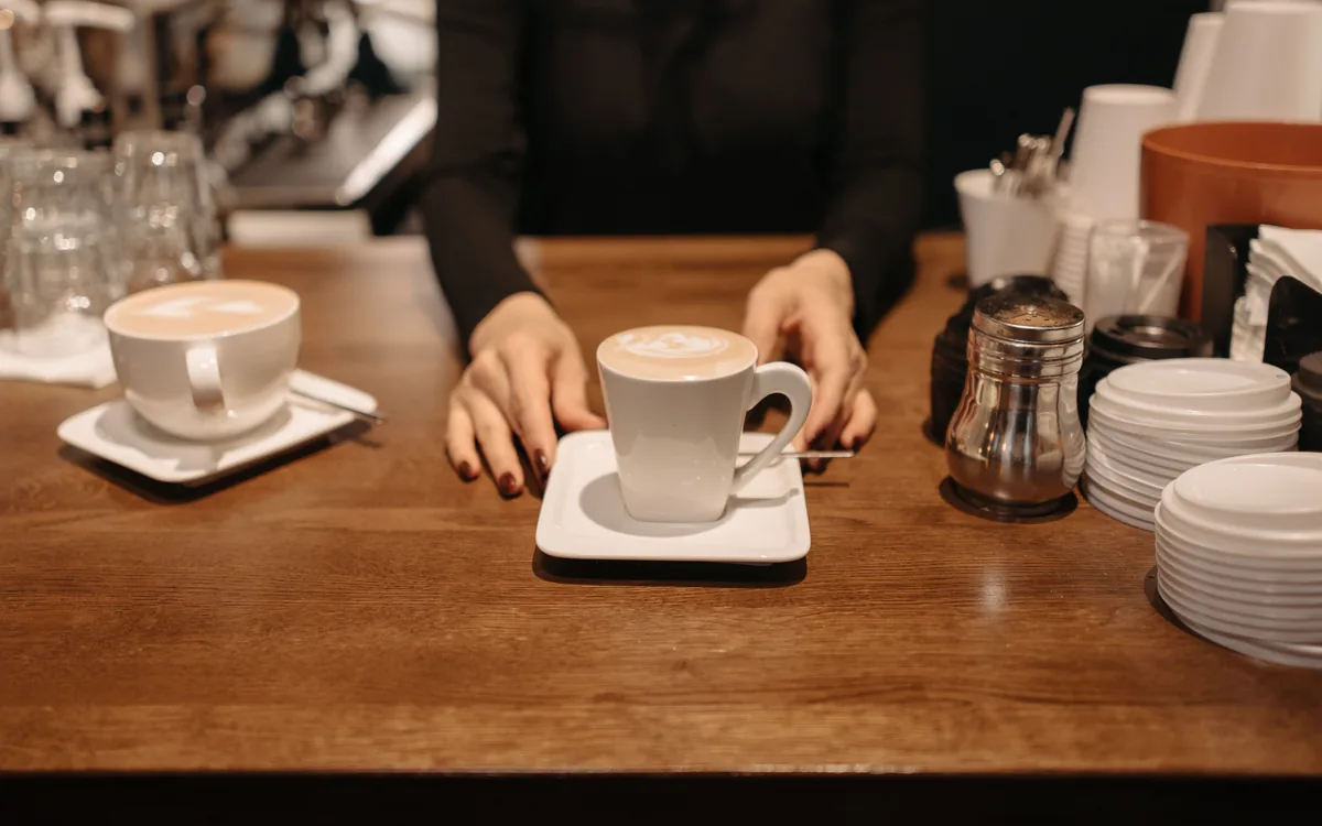 A server placing a cup of coffee on a café counter.