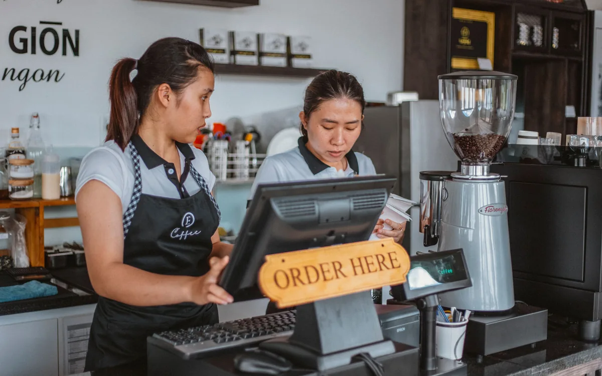 Deux employées derrière le comptoir d’un café, près de la caisse et du moulin à café.